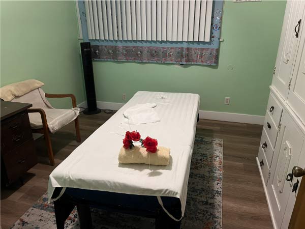 Spacious and private massage therapy room in Fresno featuring a comfortable bed, white cabinets, and a calming green atmosphere for pain relief.