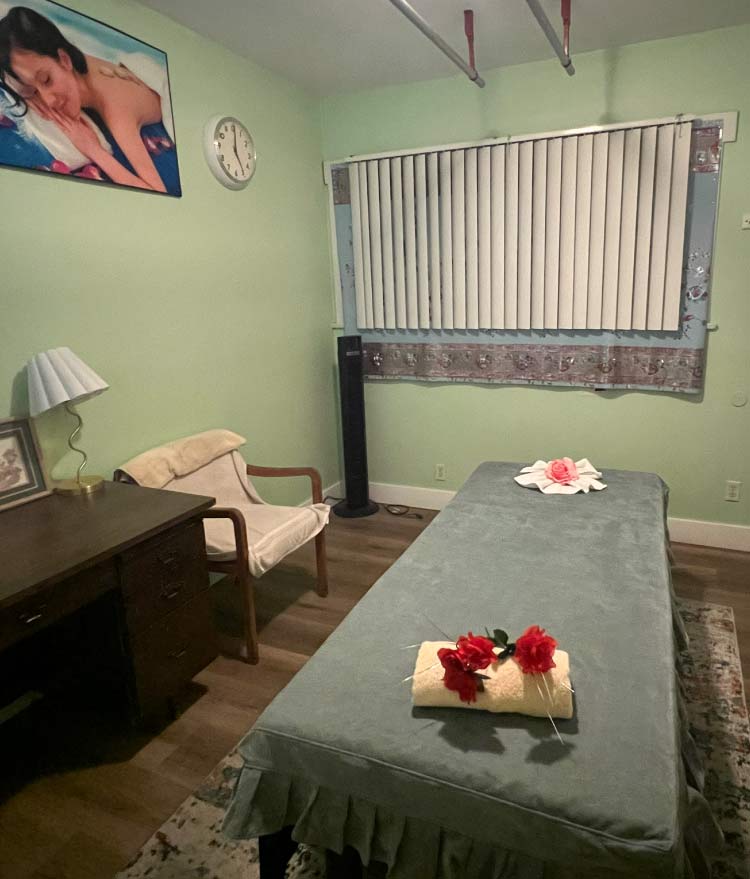 Clean and private massage spa room in Fresno prepared with fresh grey linens and red flowers for a relaxing Swedish or Deep Tissue session.