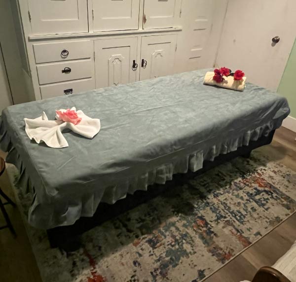 Professional massage therapy table prepared with clean grey linens and floral decor for Swedish, Thai, or Deep Tissue pain relief sessions in a private room.