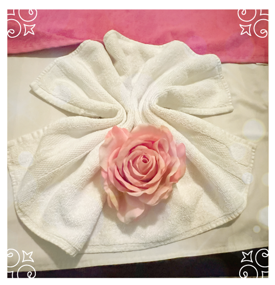 Decorative towel art with a pink rose on a massage bed, showcasing the caring service and "Golden Hands"  approach to healing.