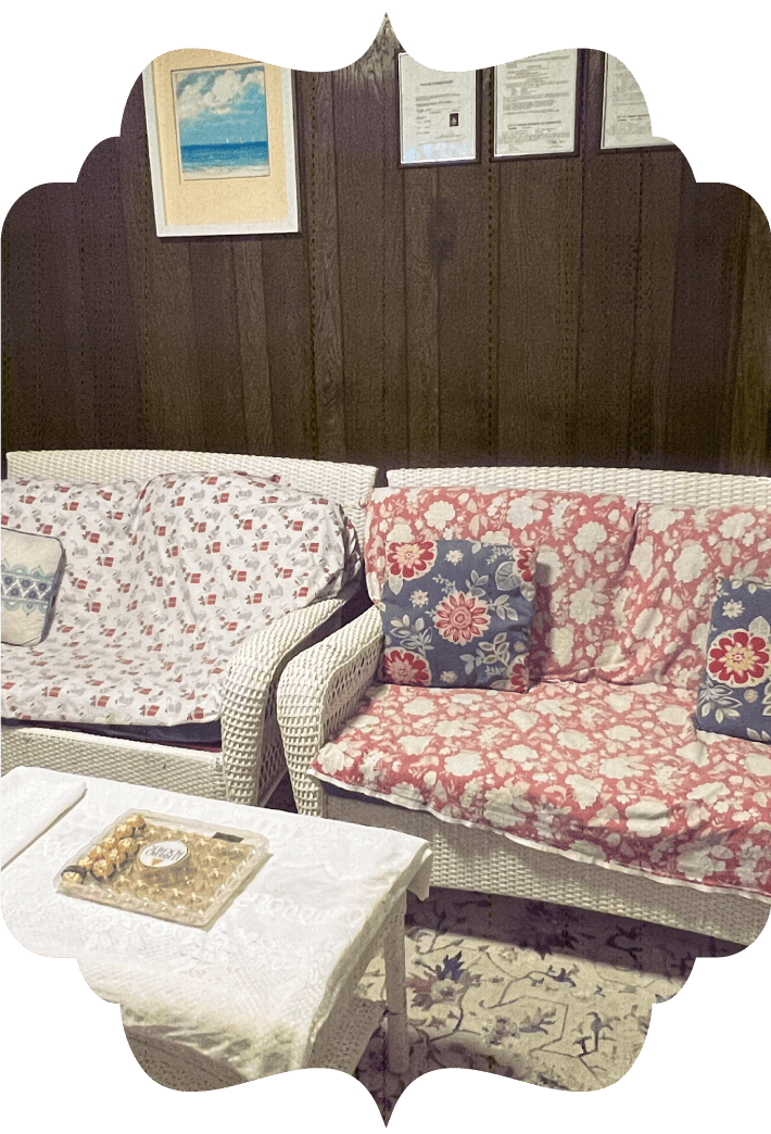 Comfortable waiting area at Golden Hands Massage in Fresno featuring wicker seating, chocolates, and framed certificates on a wood-paneled wall, creating a welcoming atmosphere.